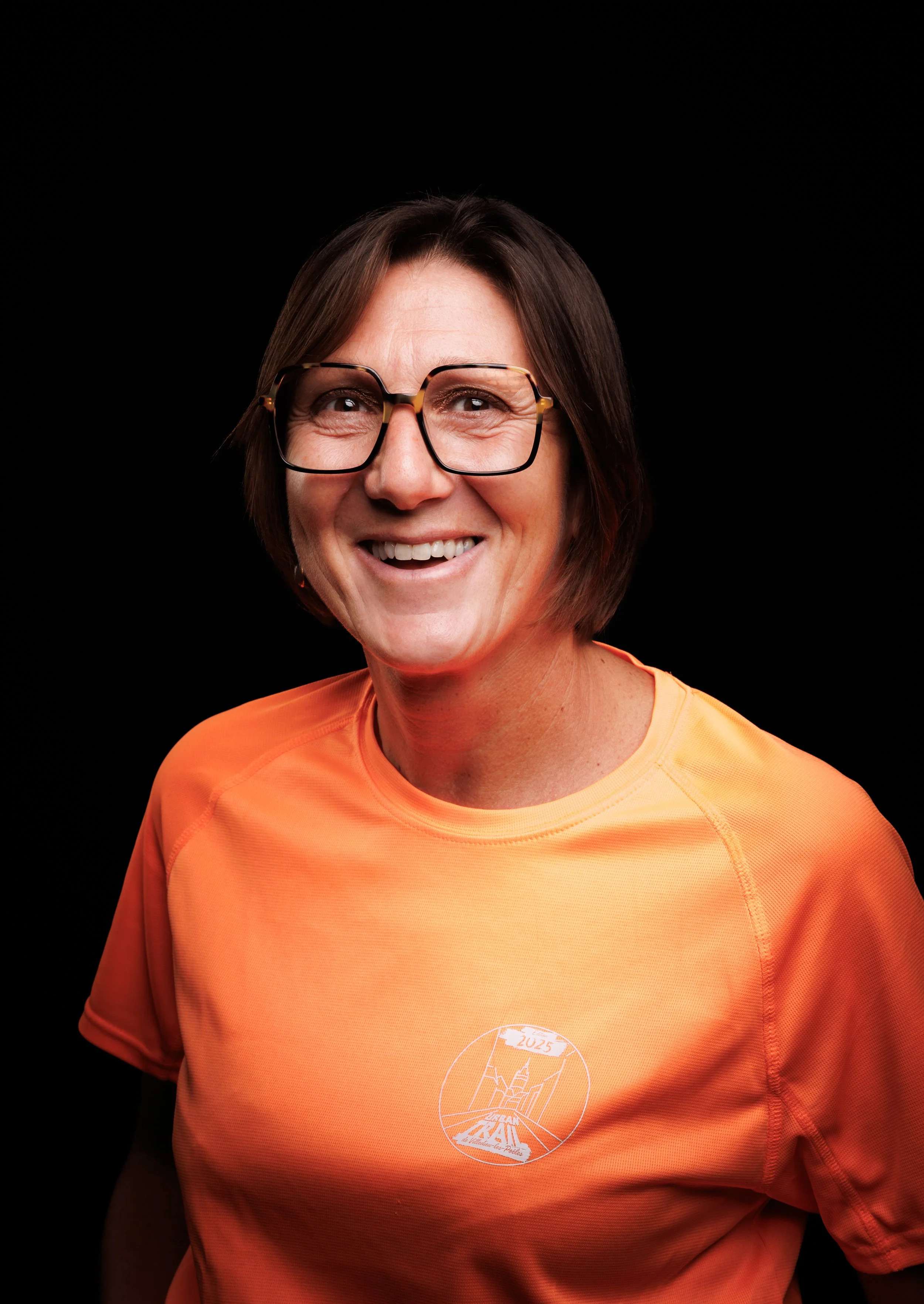 Une grande foule de personnes rassemblées pour un événement ou une course, avec un homme au centre s'adressant à la foule, sous un grand arc gonflable noir et rouge sur la droite.