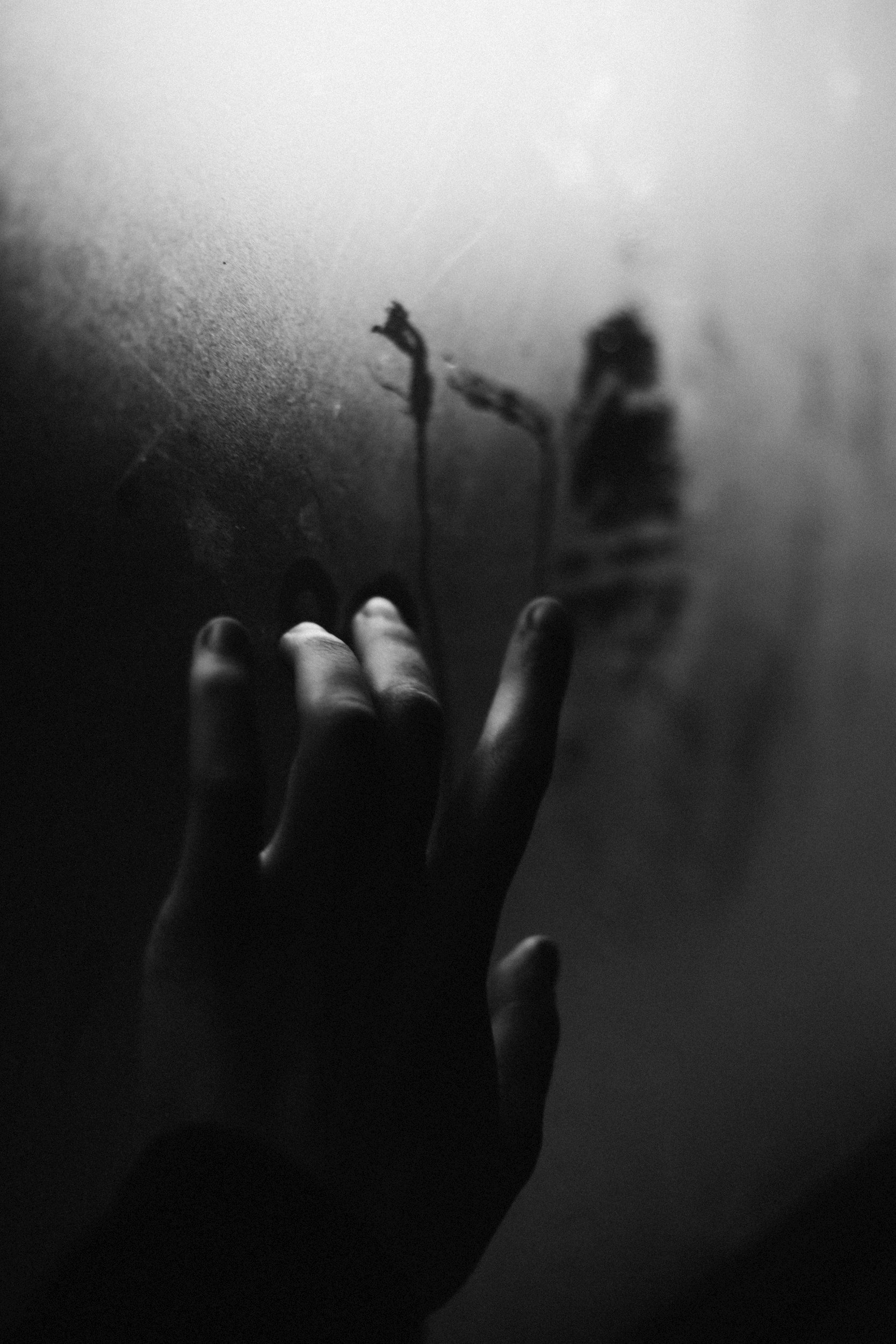 A hand reaching out to write on a foggy or frosted glass surface with a finger.