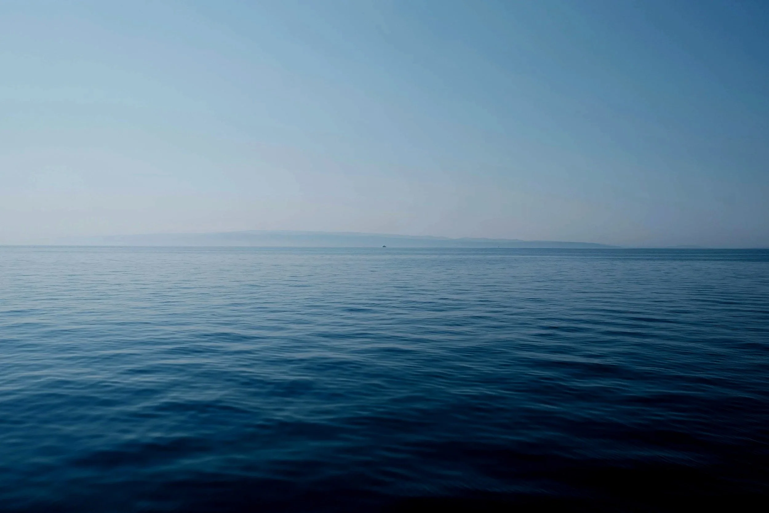 Calm ocean water with distant landmass and blue sky.