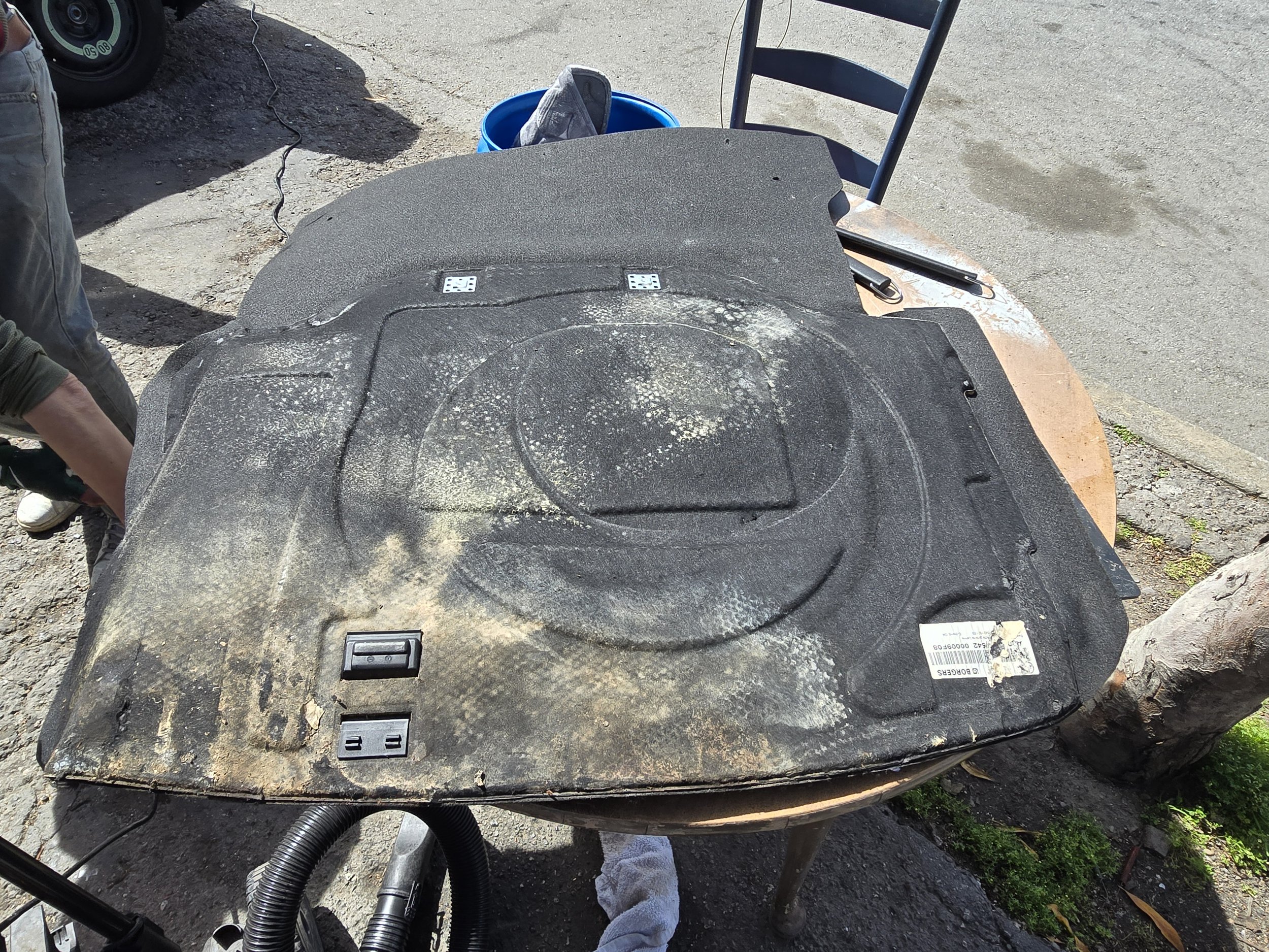 A black, dusty, large piece of equipment or machinery part with electrical outlets and switches on a wooden table outdoors.