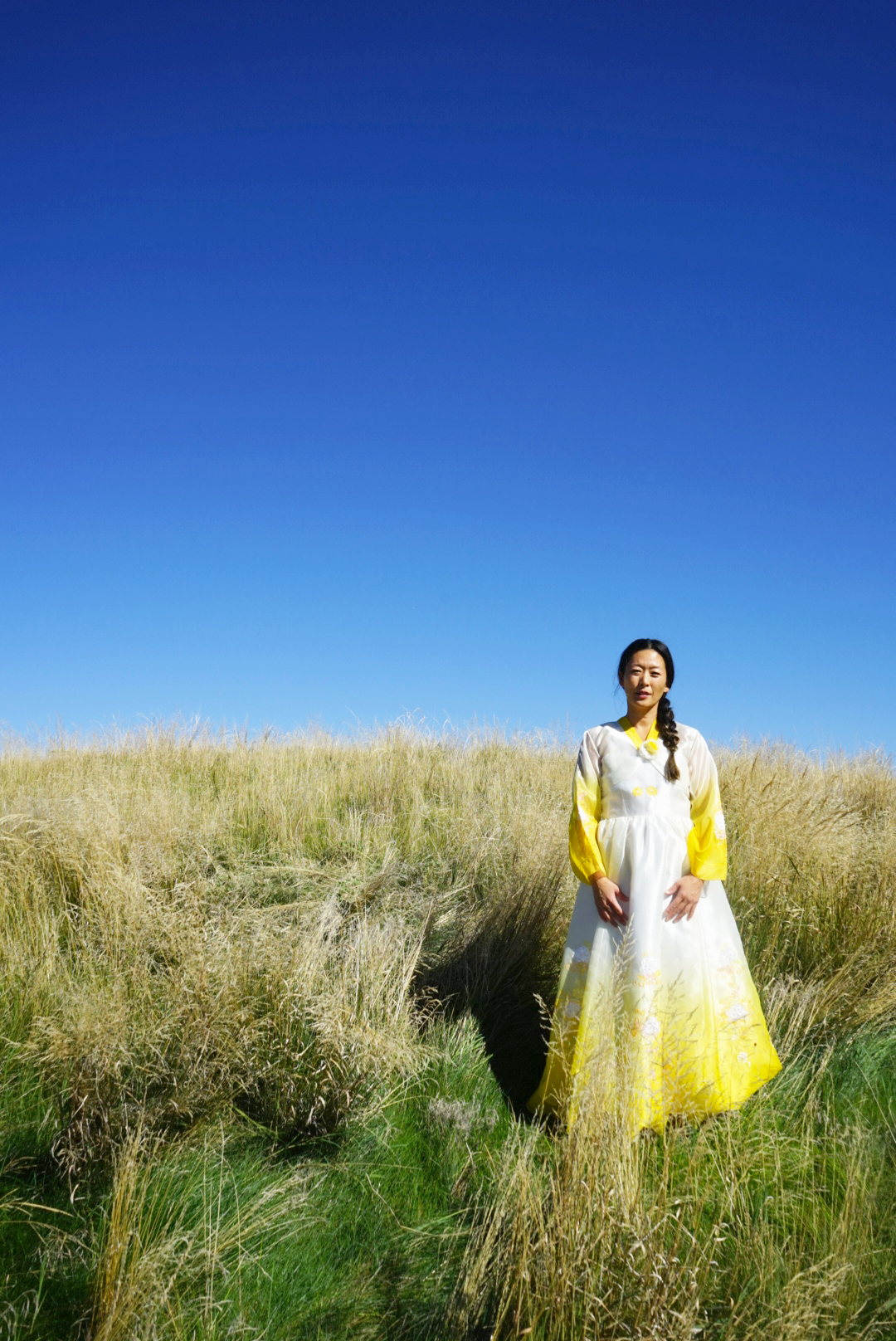 Portrait of Hannah Abuzaineh wearing a traditional Korean hanbok in coastal grasslands for the In Time photo essay exploring Korean identity, memory, and belonging.