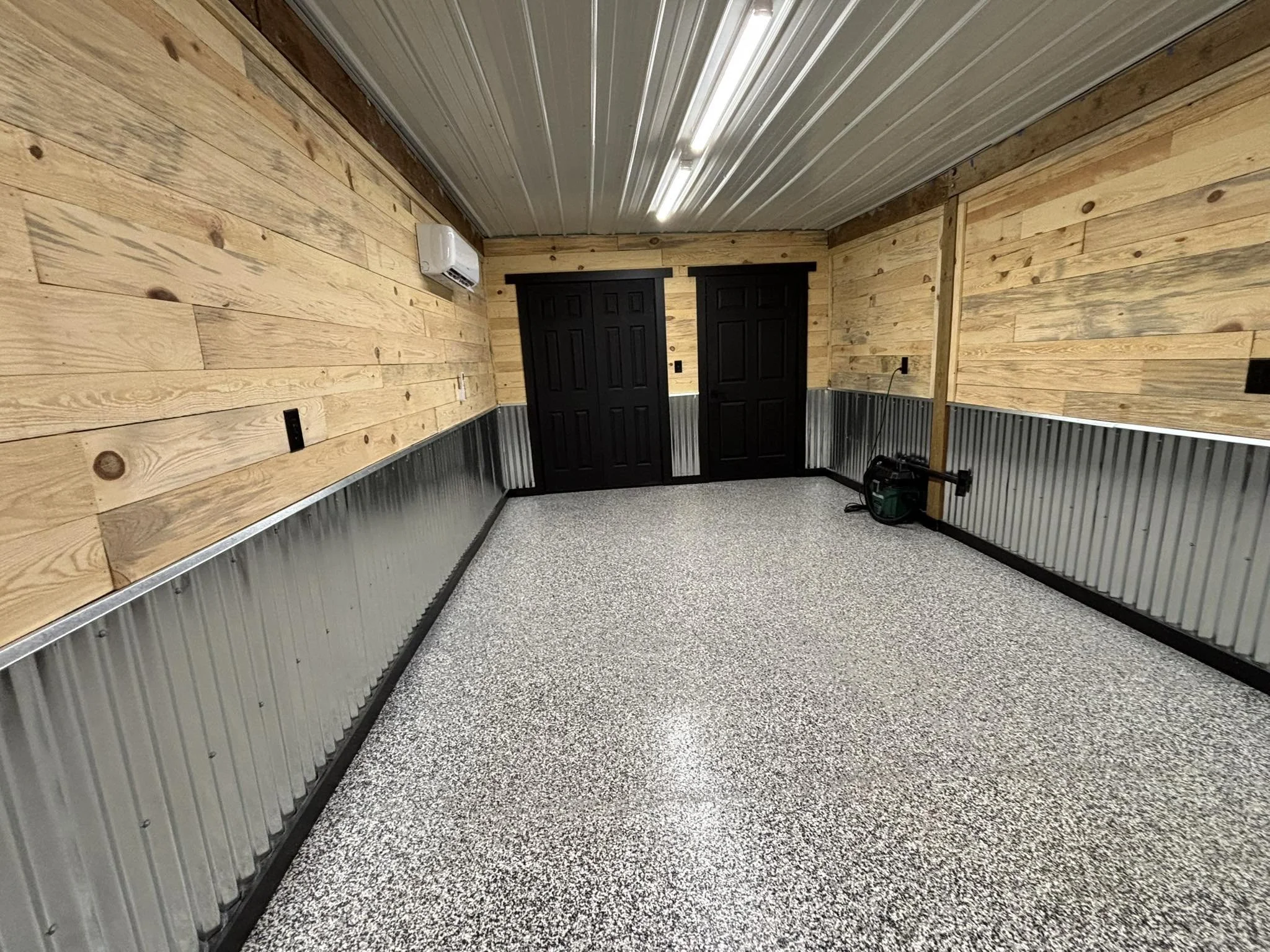 Interior of a building under construction with rustic pine paneled wall, arched ceiling framework, and construction tools and materials scattered on the floor.