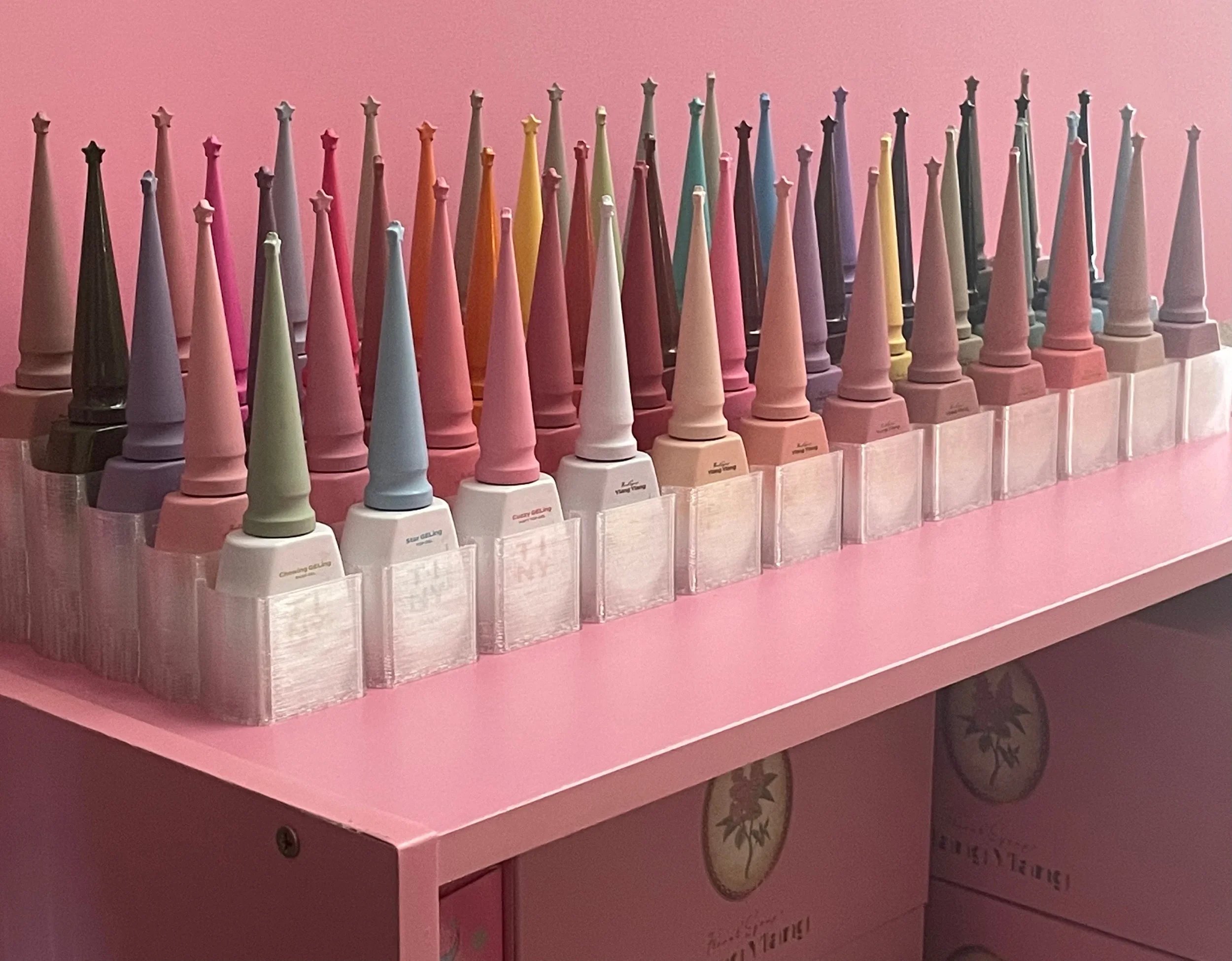 Colorful nail polish bottles arranged in rows on a pink display table.