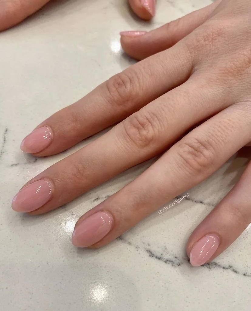 Close-up of a hand with neatly manicured nails painted in a light pink, glossy polish resting on a marble surface.