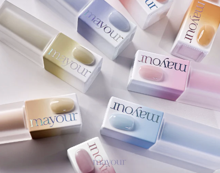 Multiple Mayour lip glosses in pastel shades, each with a small amount of gloss inside, arranged on a white surface.