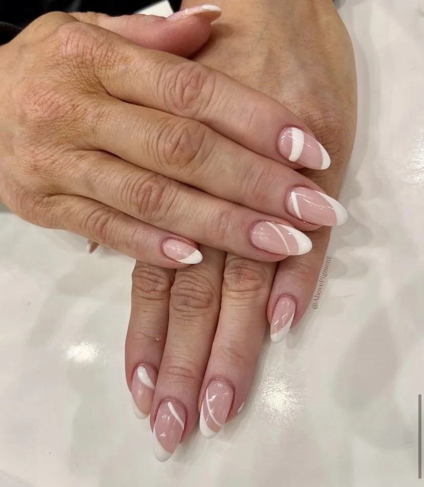 Close-up of manicured hands with French tip nails featuring white tips and subtle pink swirl designs.