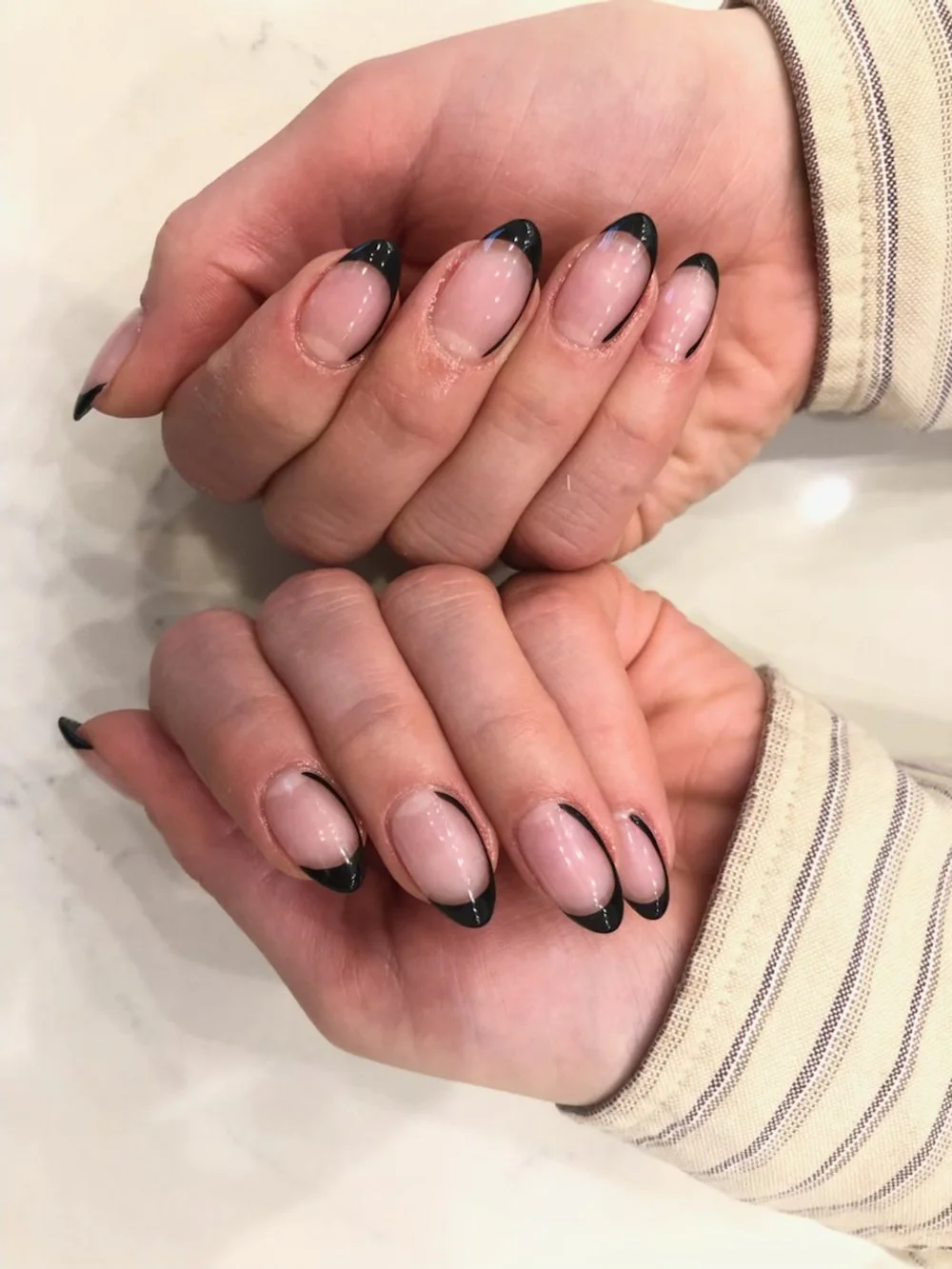 Close-up of hands with well-manicured nails featuring a nude base with black French tips.