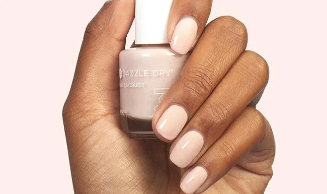 Hand with light pink painted nails holding a bottle of pink nail polish.