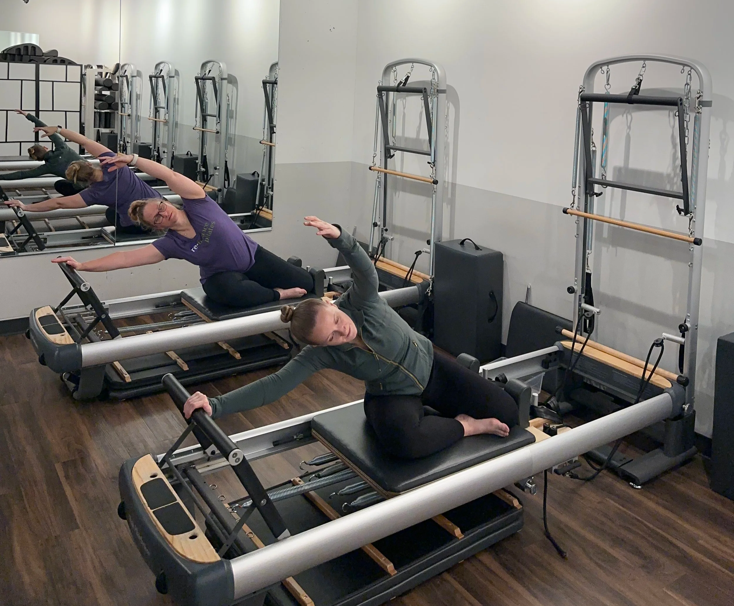 Two people performing Pilates reformer exercises with controlled movement and coordinated breath. Two individuals performing Pilates reformer exercises together during a guided session.