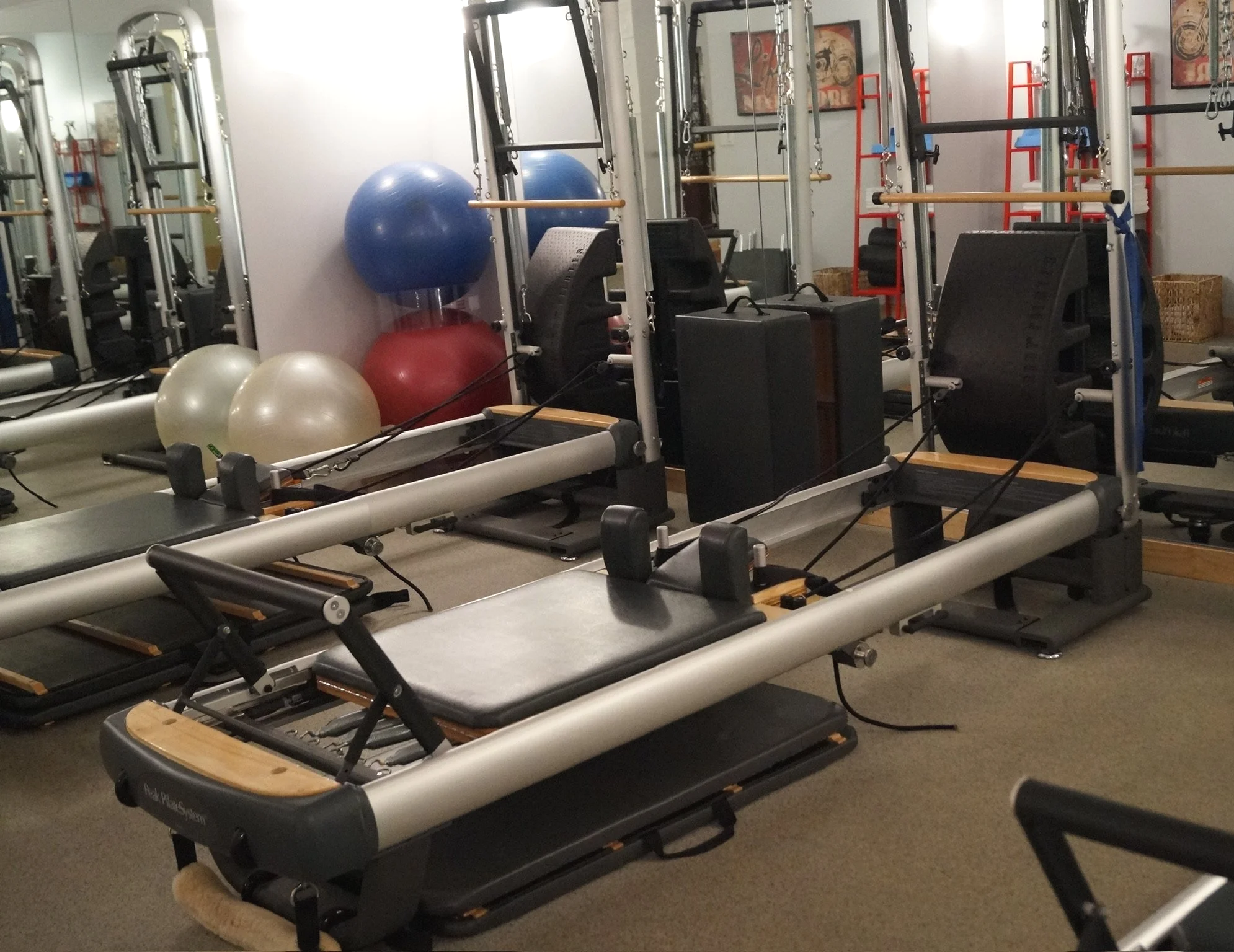 This is an image of a pilates reformer. A common machine used to teach pilates and practice exercises in order to achieve better fitness. Originally created by Joseph Plates. Yoga balls and mirrors are in the background of this photo.