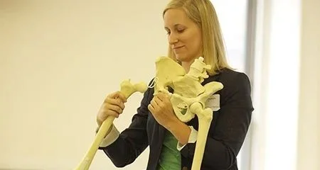 Instructor-led course with a physical therapist holding a skeleton model to teach anatomy and movement principles.
