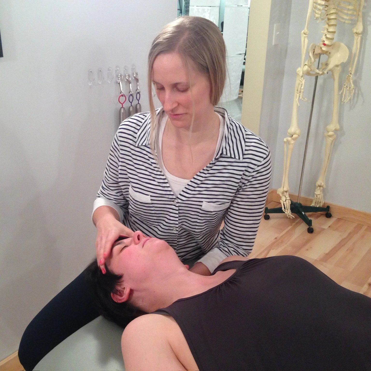 Dr. Sarah Petrich has a patient laying on a table. SHe is helping the patient with a neck injury and pain. The patient is arching their neck in to Sarah's hands. The photo was taken at Studio U.