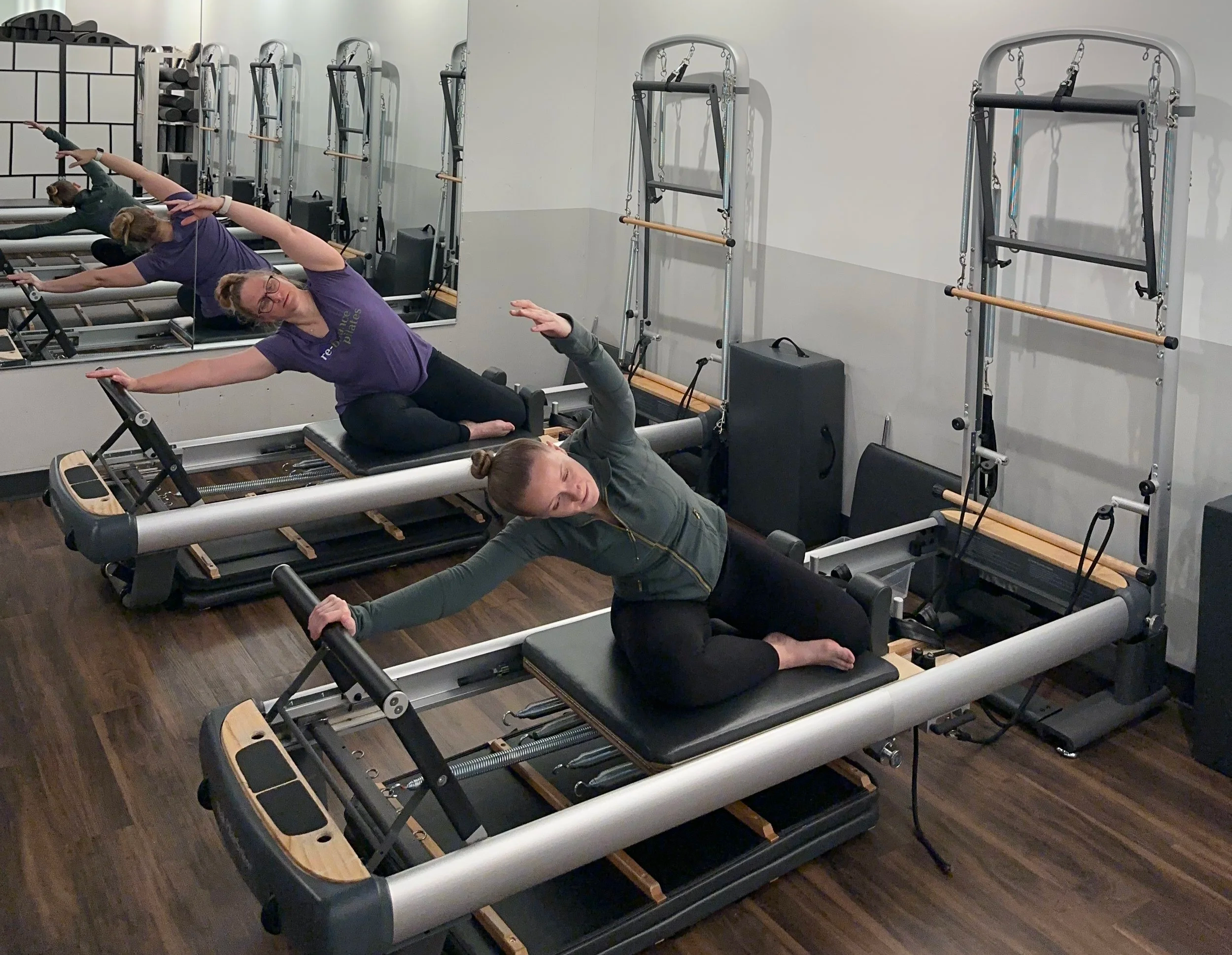 This photo has 2 people taking pilates class together. They are on the reformer pushing the carriage out so that they can stretch the side of their body. Feels good and fun to do in a class setting.