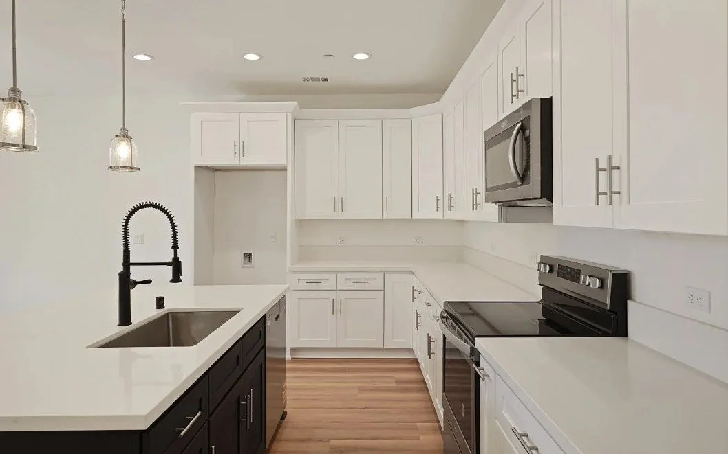 Modern kitchen with white cabinets, black island, stainless steel appliances, and wood flooring.