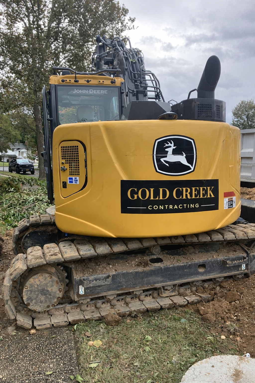A person operating a red mini excavator on a dirt surface in a wooded area, wearing a yellow safety vest and dark clothing.