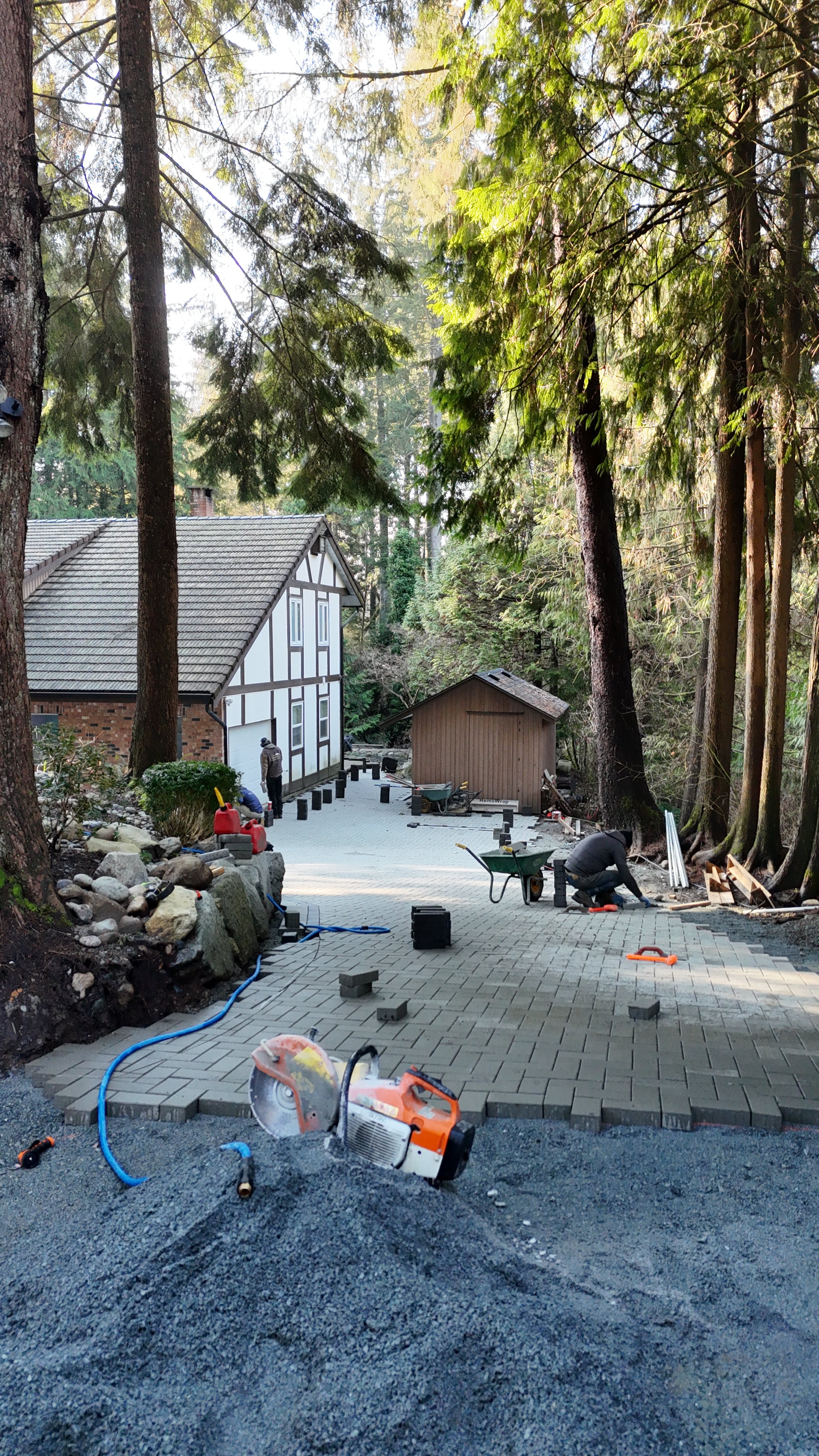 Backyard with stamped concrete patio, artificial grass patch, wooden fence, and trees in the background.