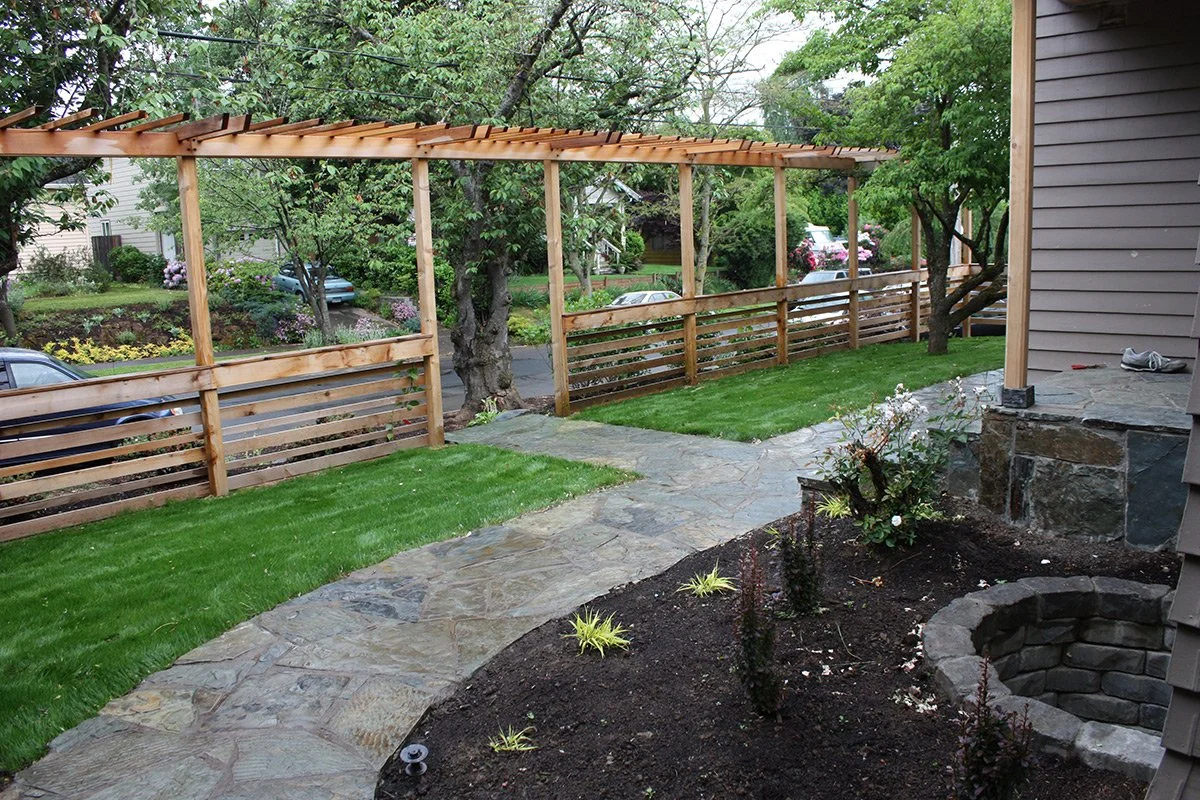 Backyard with new wooden fence, stone pathway, green grass, and garden bed with plants and flowers.