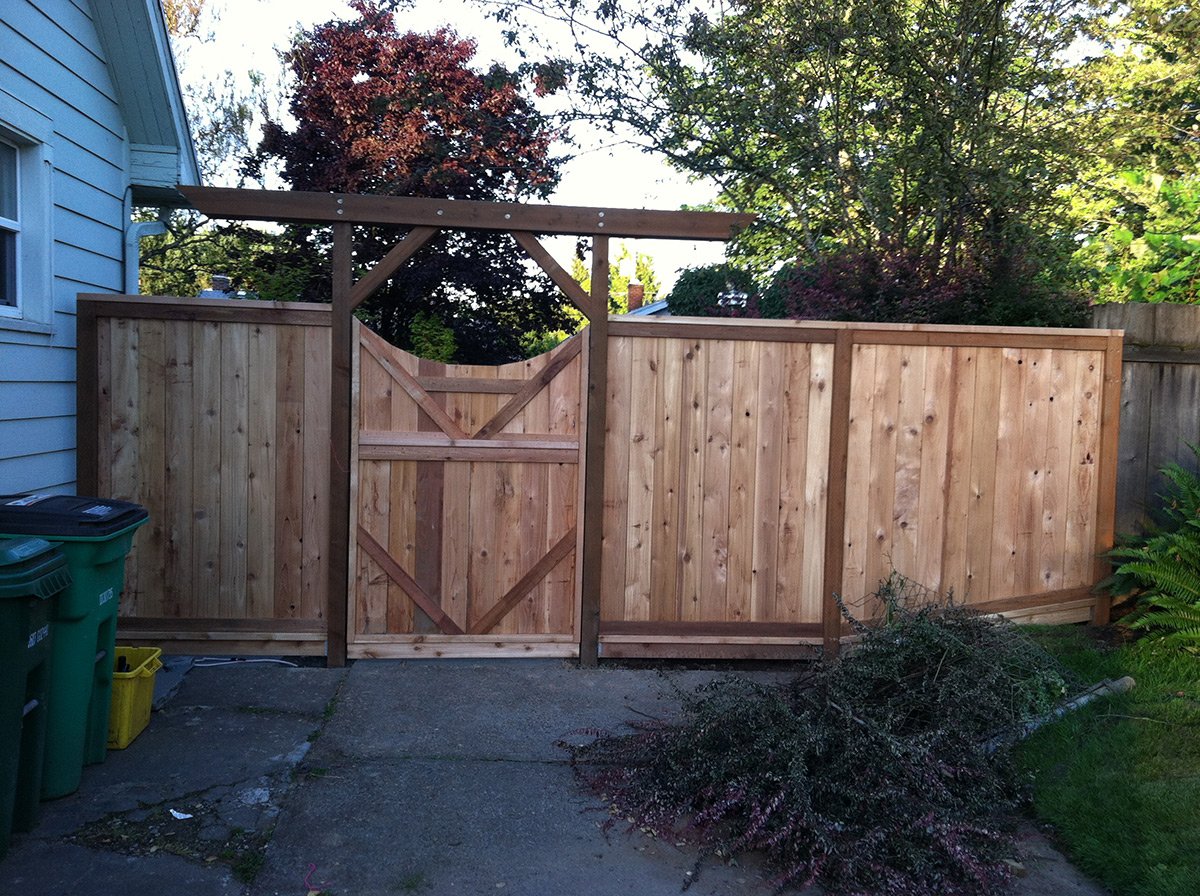 A backyard wooden fence being built with a partially installed gate, surrounded by trees and greenery.