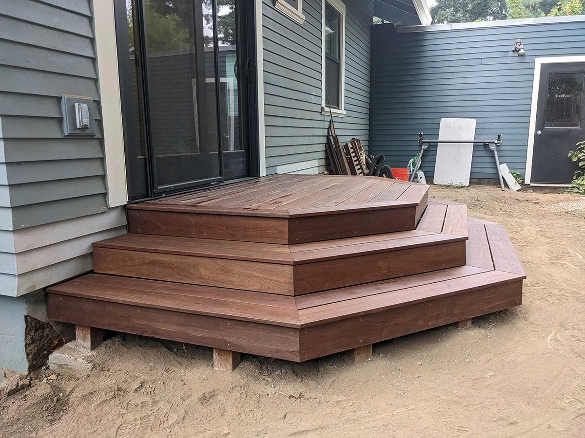 New wooden deck with steps attached to the house exterior, with construction materials and tools in the background.