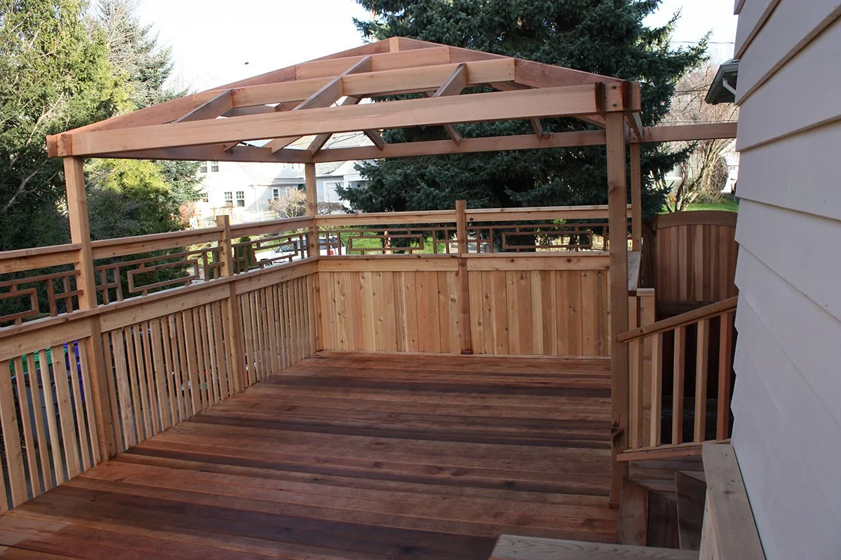 Newly built wooden deck with a railing and an incomplete roof framing in a residential backyard.