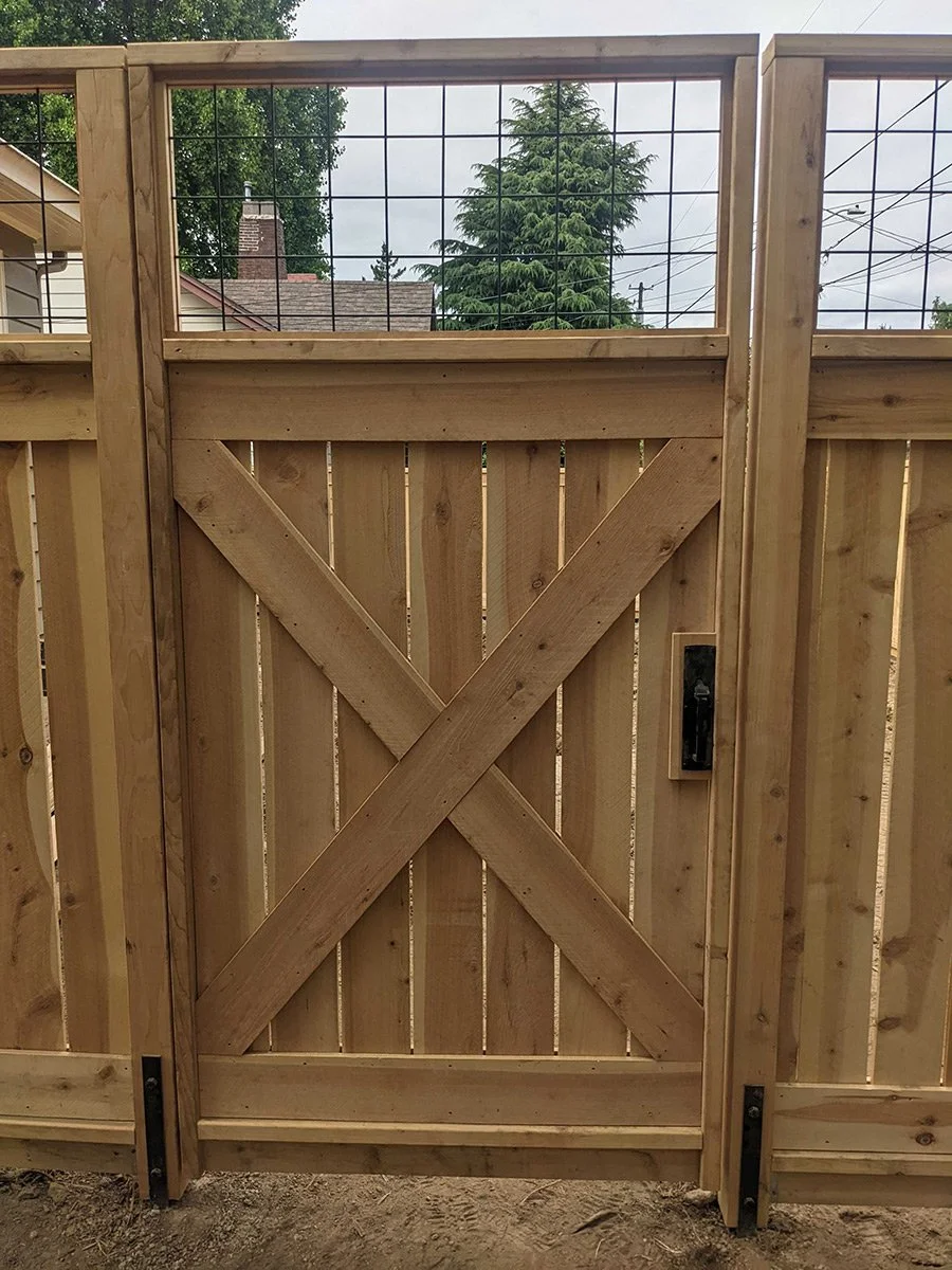 Wooden gate with wire mesh panels in a fenced backyard.