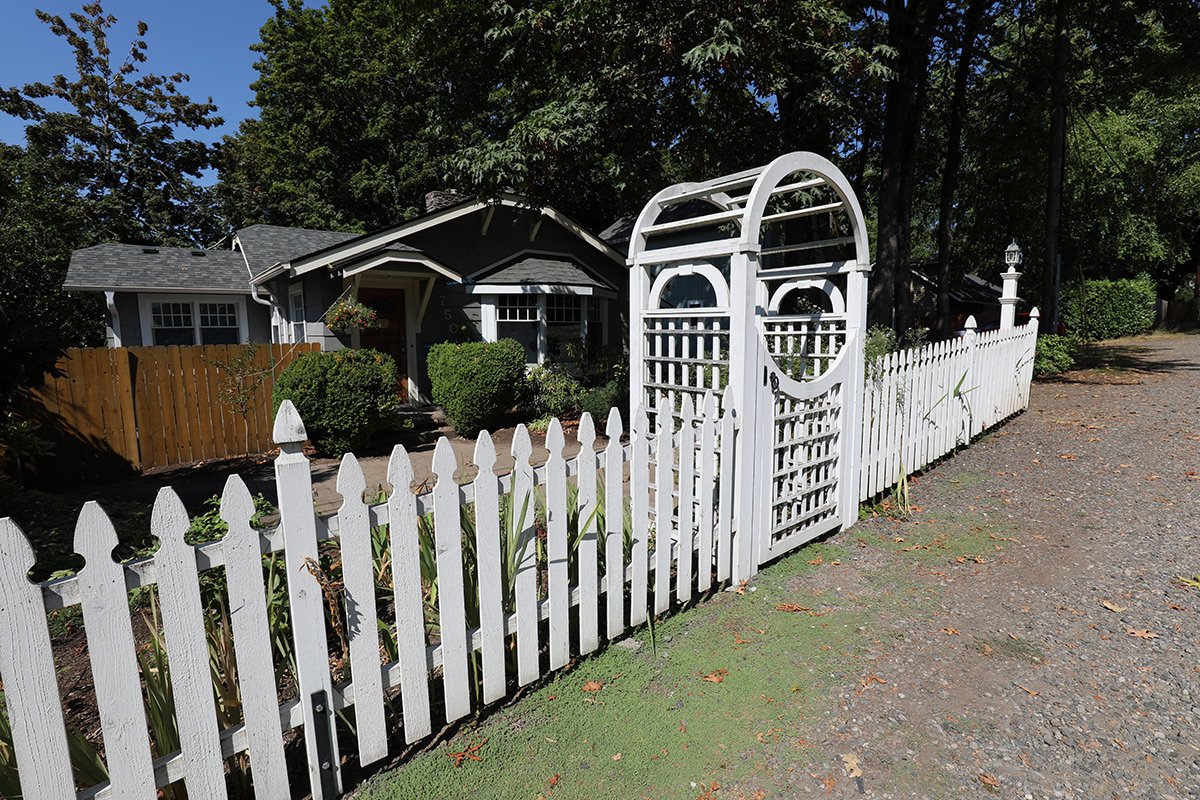 White picket fence and arbor surrounding a front yard with a house in the background