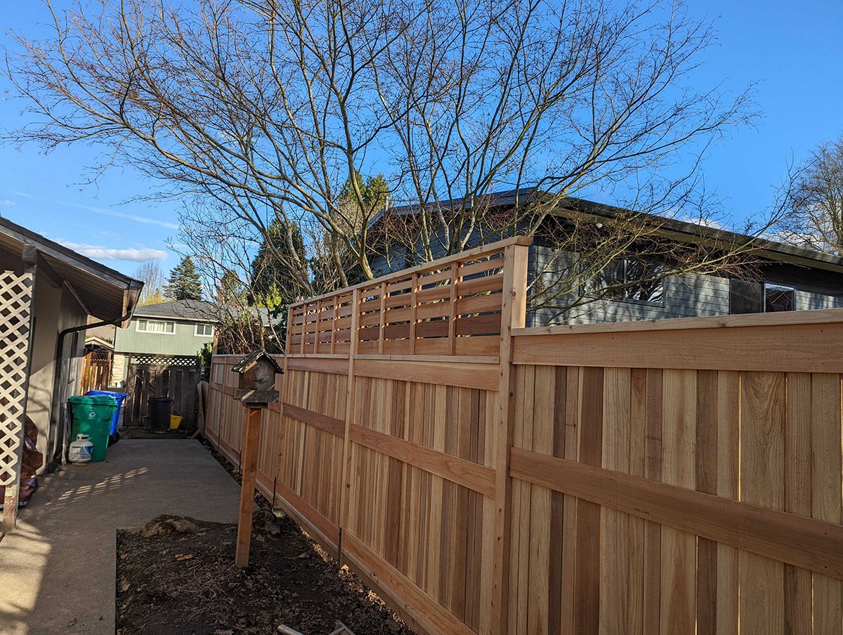 New wooden fence being built in a backyard, with a clear blue sky and a tree with no leaves.