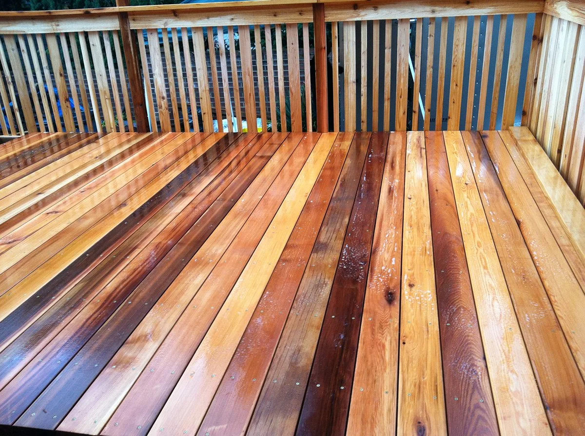 Close-up of a wooden deck with polished, stained floorboards and a railing in the background.