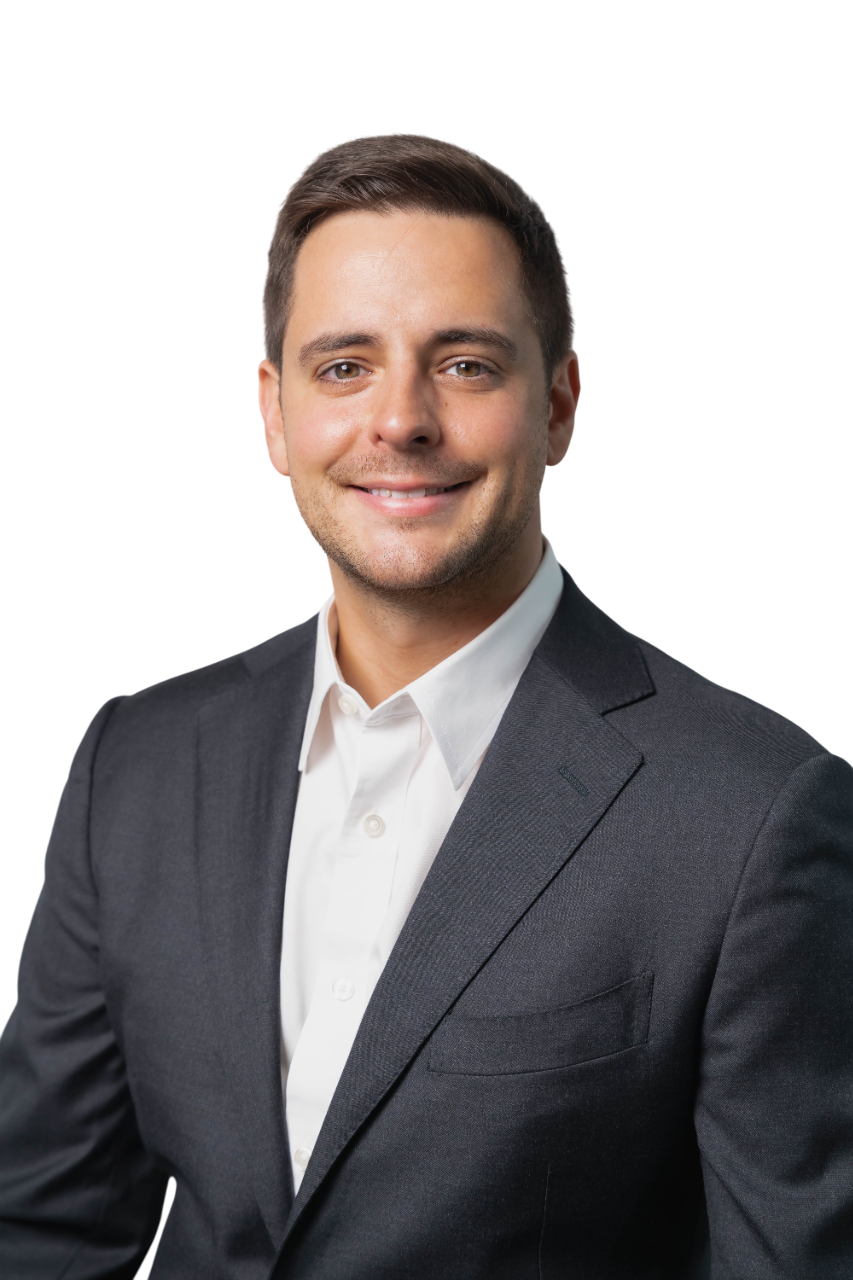 Professional portrait of a young man with short dark hair, wearing a dark gray suit and white shirt, smiling against a white background.