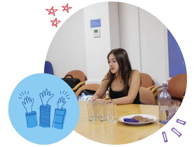 A young woman sitting at a table with empty glasses, a plate of cookies, and a water bottle, looking down with a thoughtful expression.