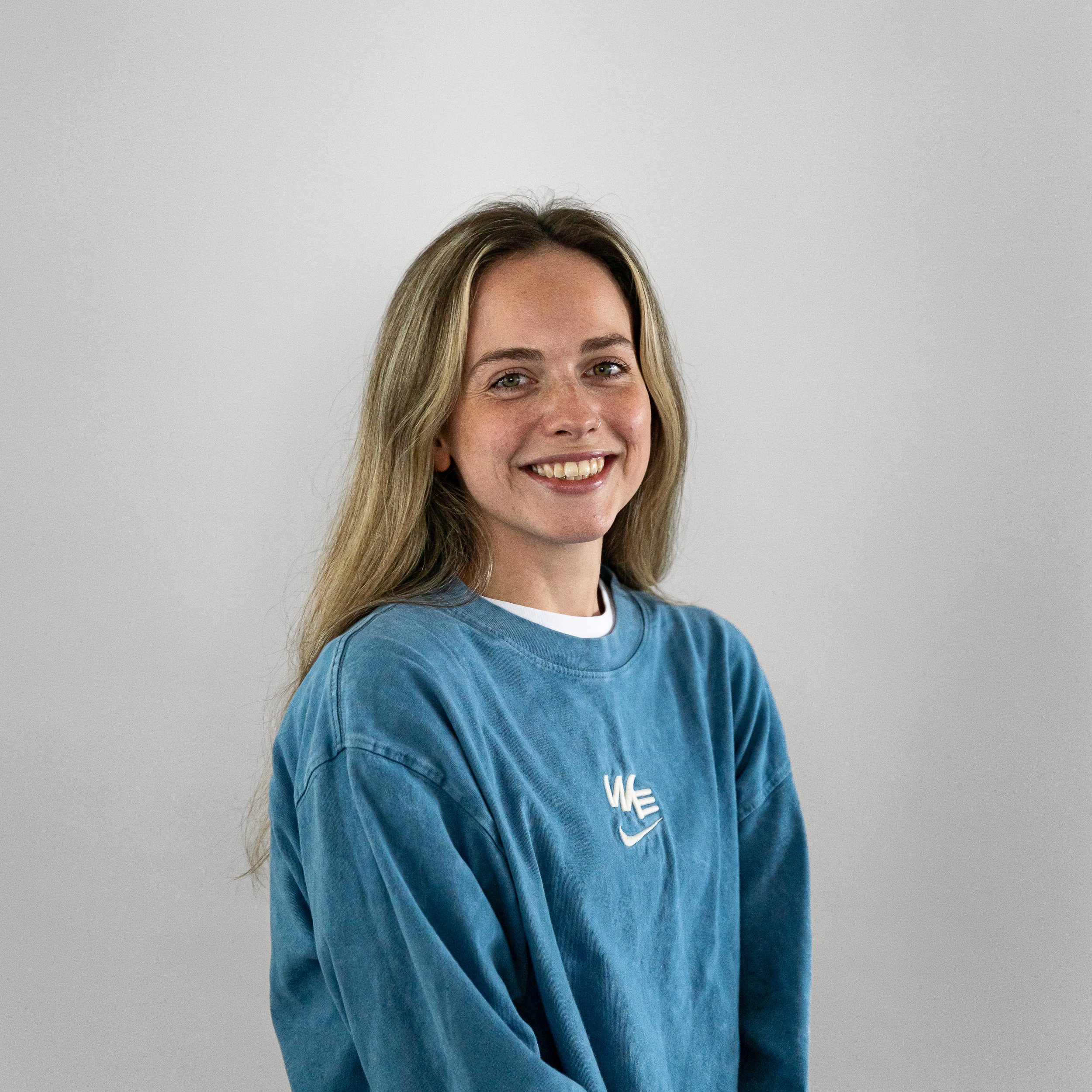 Portrait of a woman with long blonde hair, wearing a blue sweater, smiling against a plain white background.