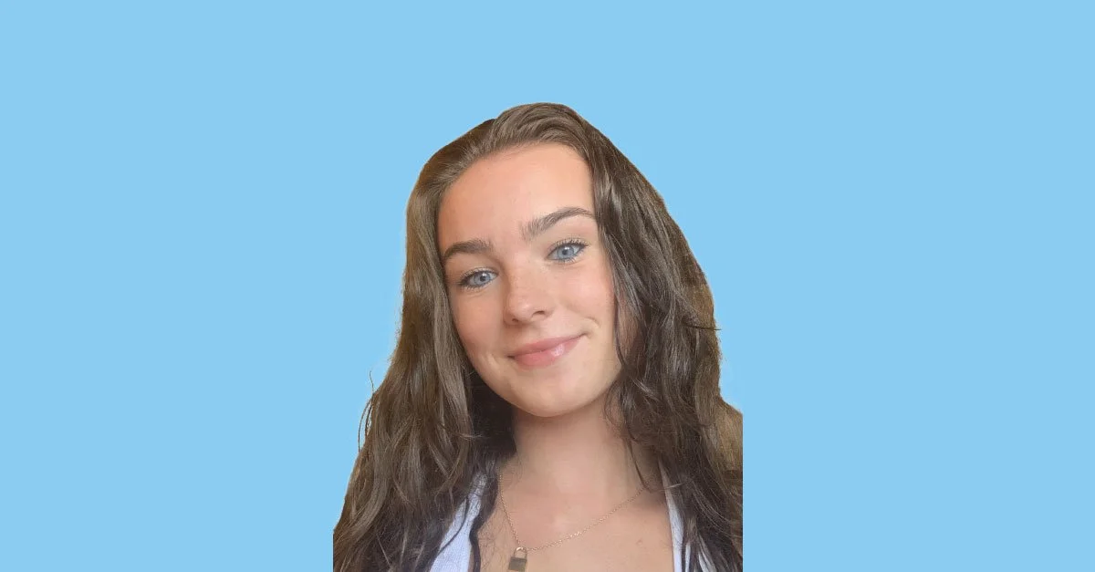 Portrait of a young woman with long brown curly hair and blue eyes smiling against a light blue background.