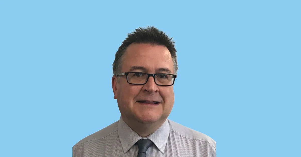 Photo of a man wearing glasses, a striped shirt, and a tie, with a light blue background.