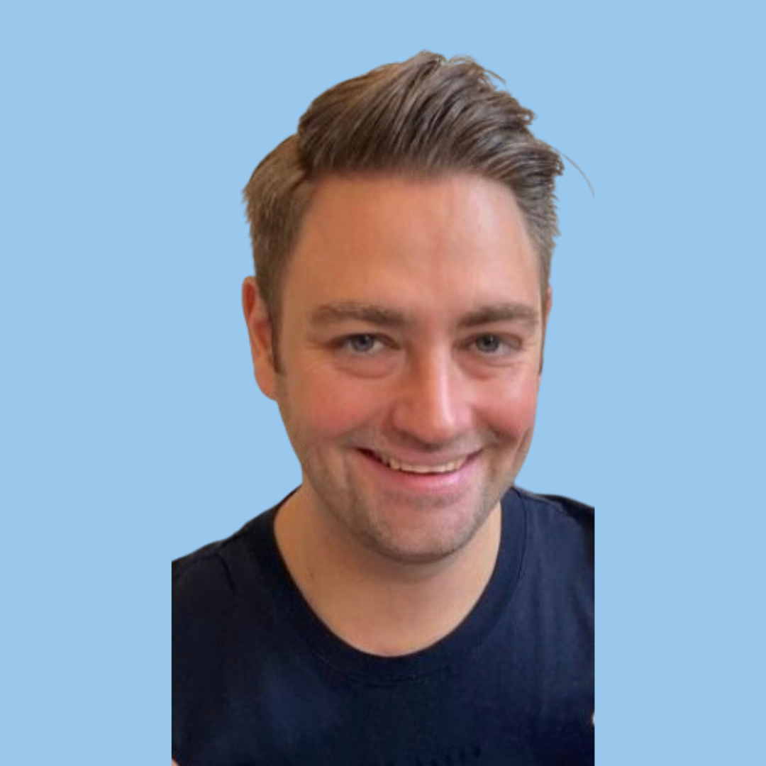 A smiling man with short brown hair, wearing a black shirt, against a light blue background.