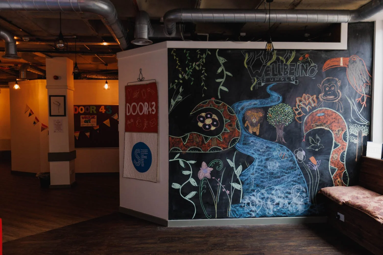 Colorful chalk drawing of jungle scene with river, trees, a flamingo, a monkey, and the words "Jungle Valley" on a black wall in a restaurant or cafe.