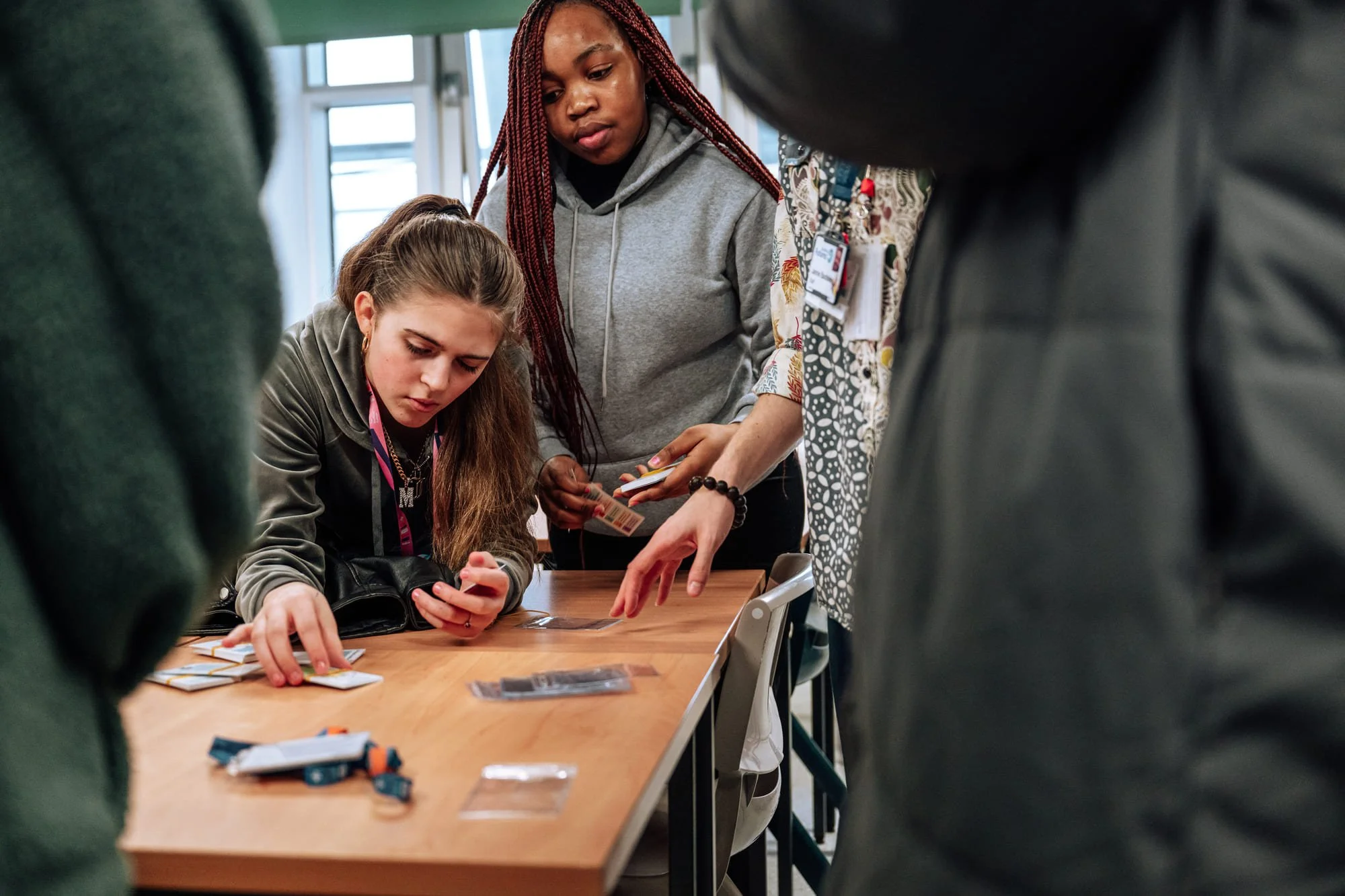 Group of young women gathered around a table playing a card game with cards and game pieces.
