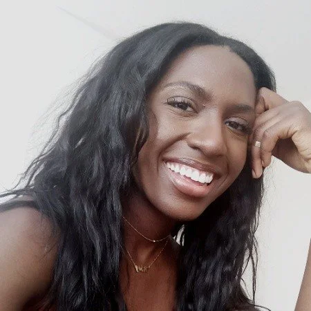 A woman with long wavy dark hair smiling, resting her head on her hand.