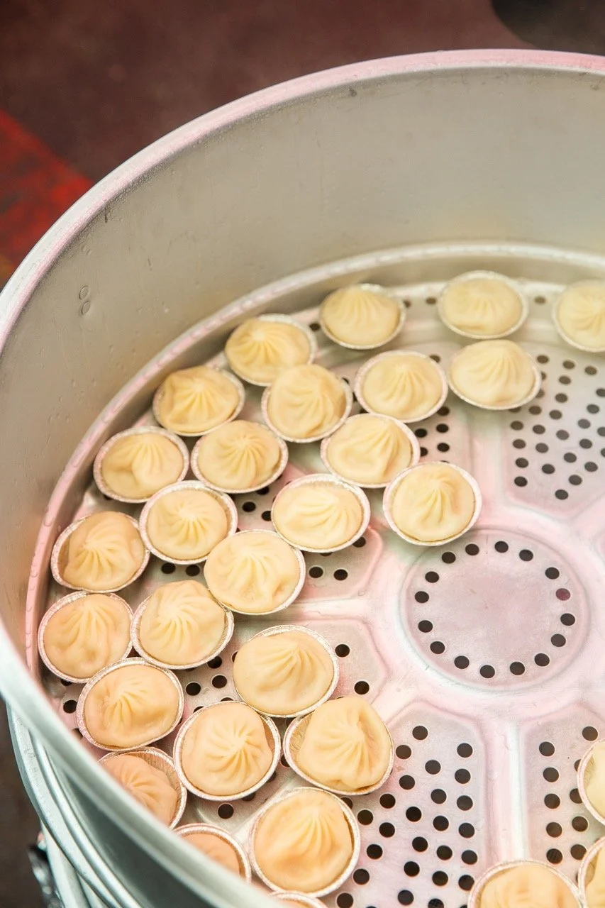 Fresh dumplings arranged in a large metal steamer, each sitting in a small foil cup with pleated tops visible.