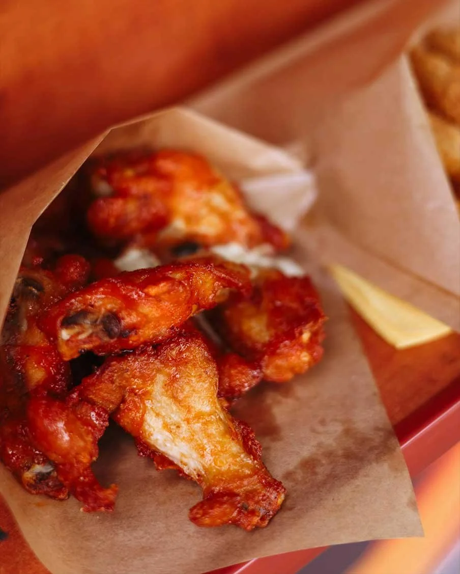 Spicy buffalo chicken wings served on parchment paper with a side of fries.