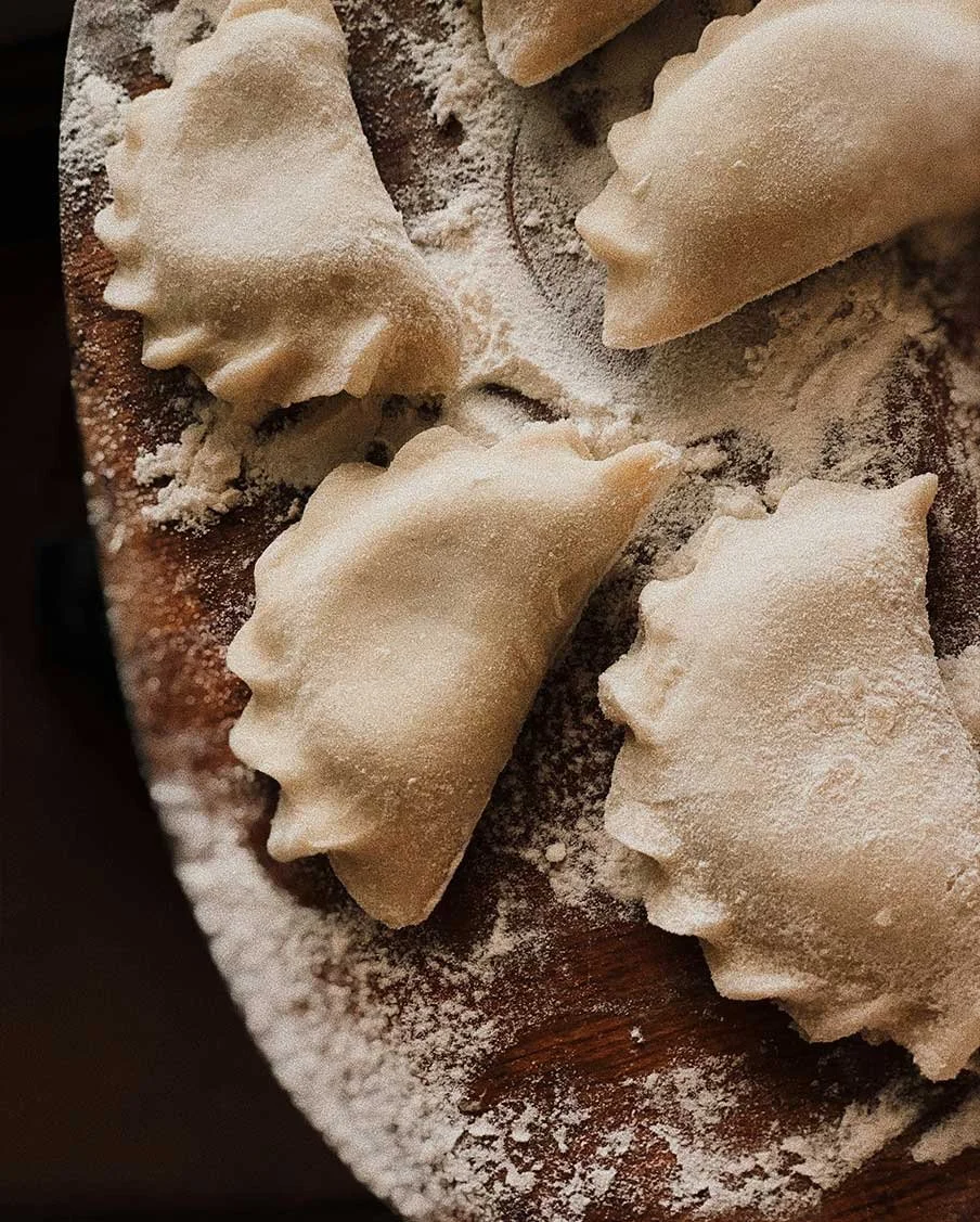 Uncooked ravioli with fluted edges dusted with flour on a wooden surface.