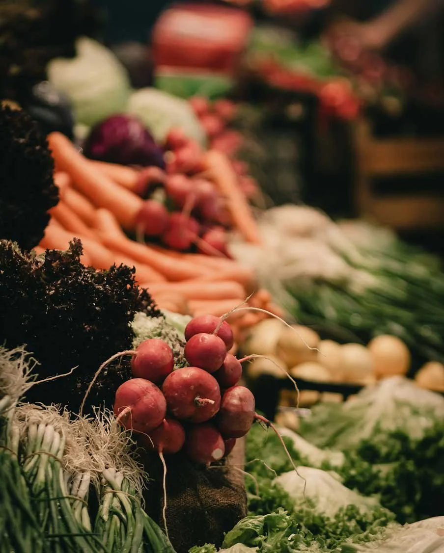 Fresh vegetables including radishes, carrots, lettuce, and onions displayed at a market stand.