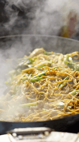  Steaming stir-fried noodles being tossed in a hot pan, with wisps of steam rising over the dish. 