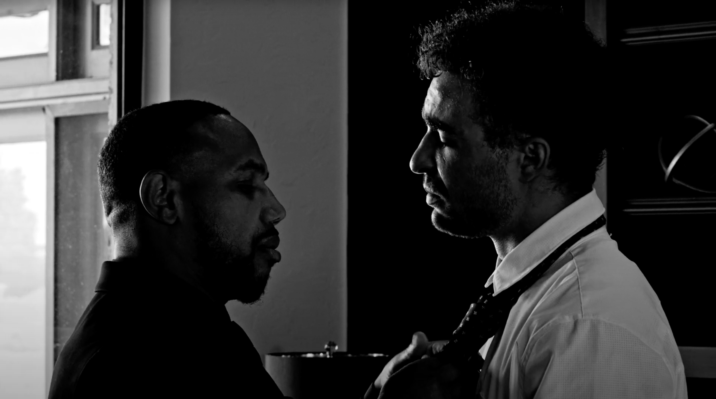 A black and white image of a doctor and a patient standing face to face in a hospital room, with the doctor wearing a stethoscope.