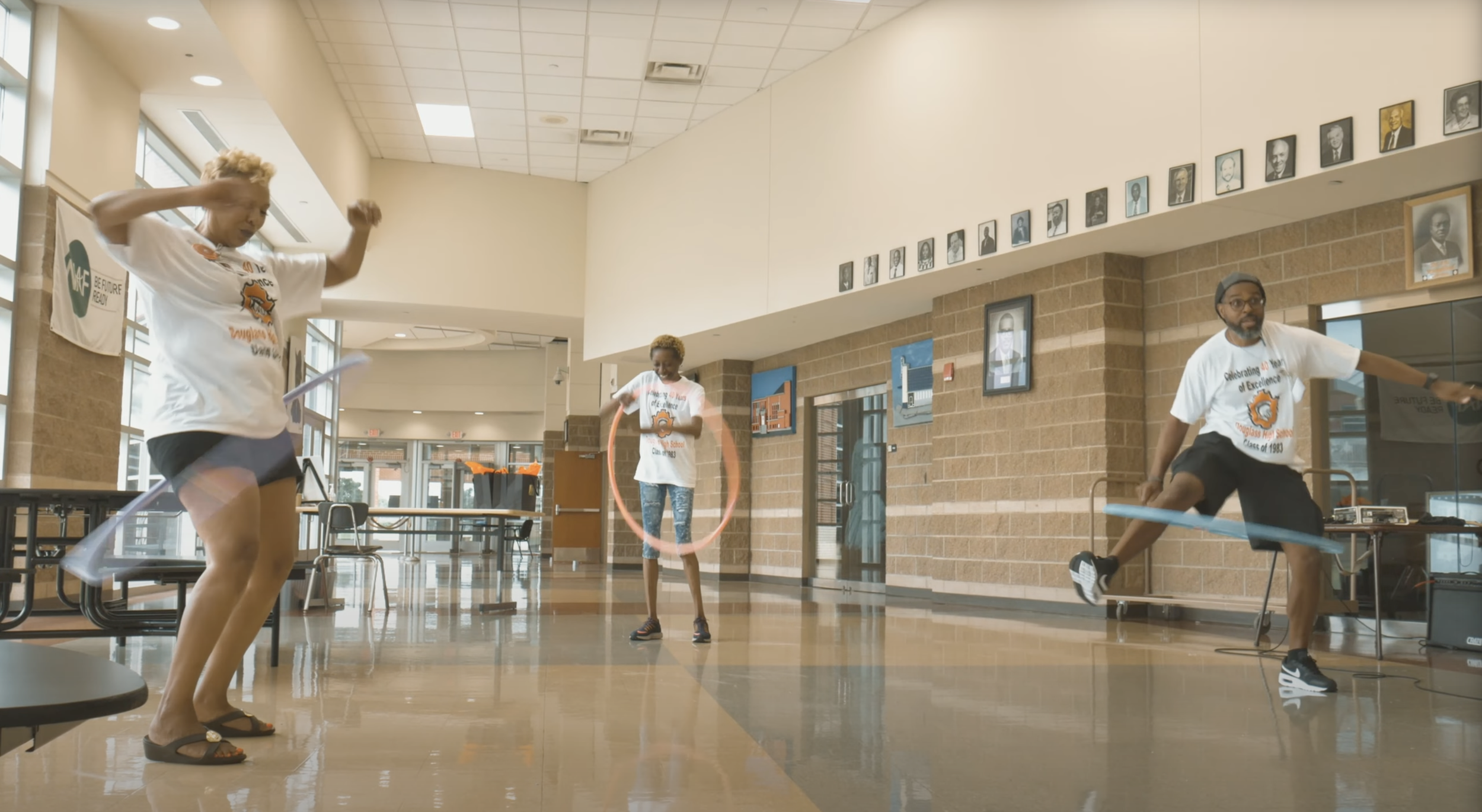 Three people playing with hula hoops indoors in a school hallway.