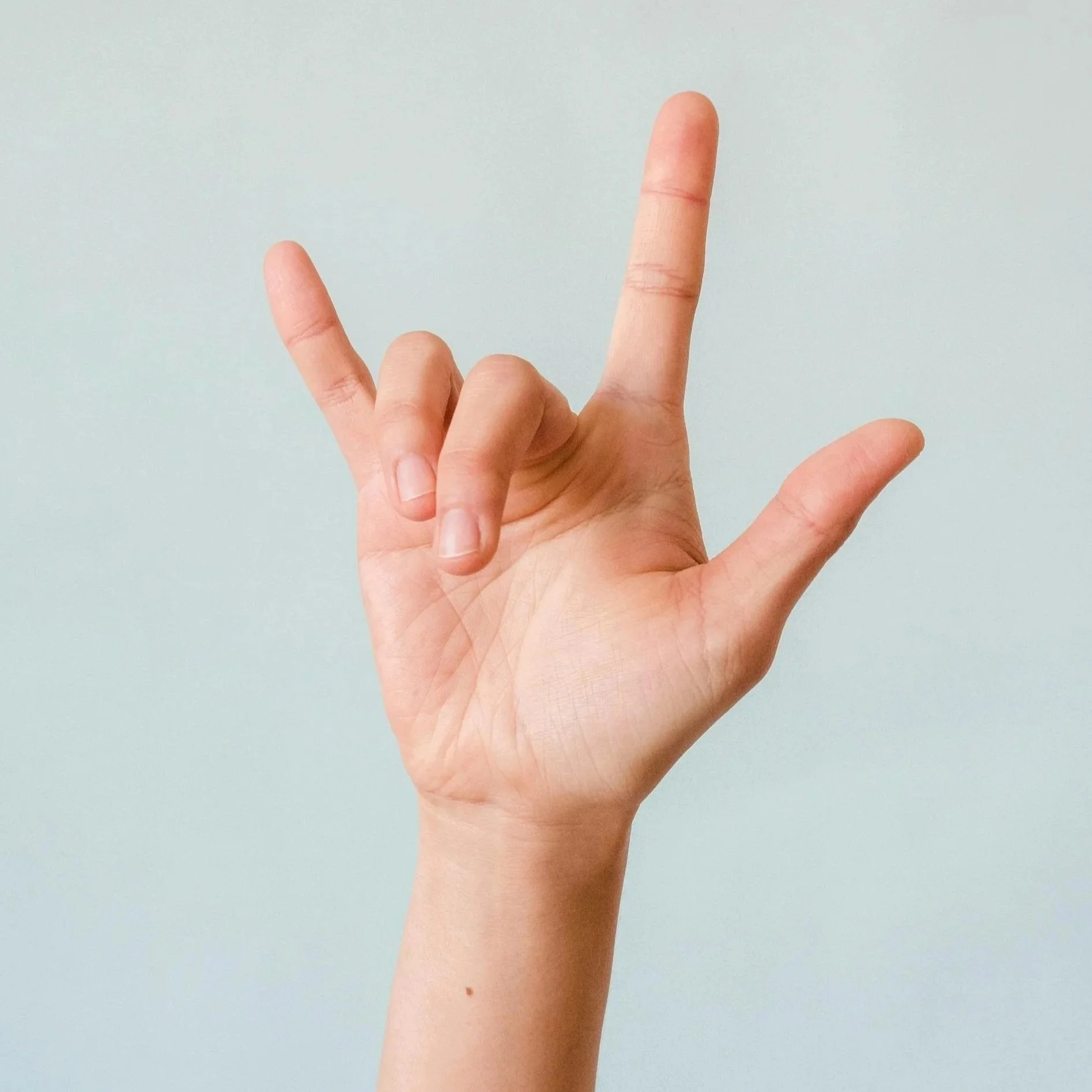 Hand making the American Sign Language sign for 'I love you' against a light blue background.