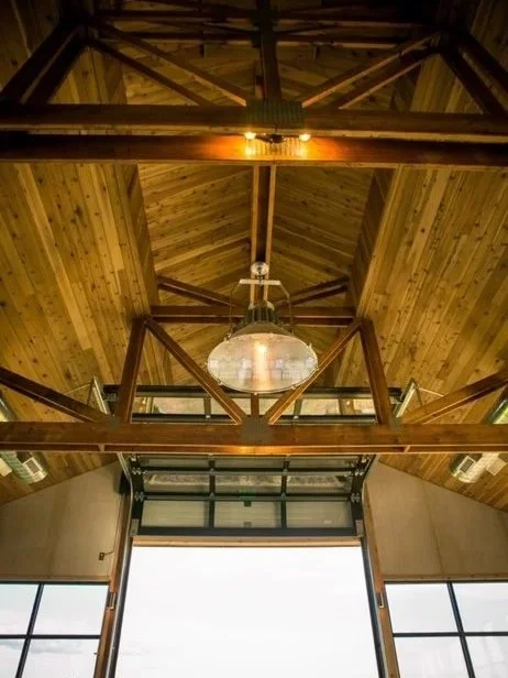 Inside view of a wooden ceiling with exposed beams and a large glass pendant light, with large windows at the bottom.