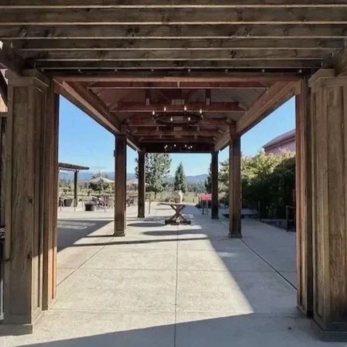 View of a draped entry area with wooden beams and columns, concrete floor, and a table in the distance, overlooking mountains and greenery.