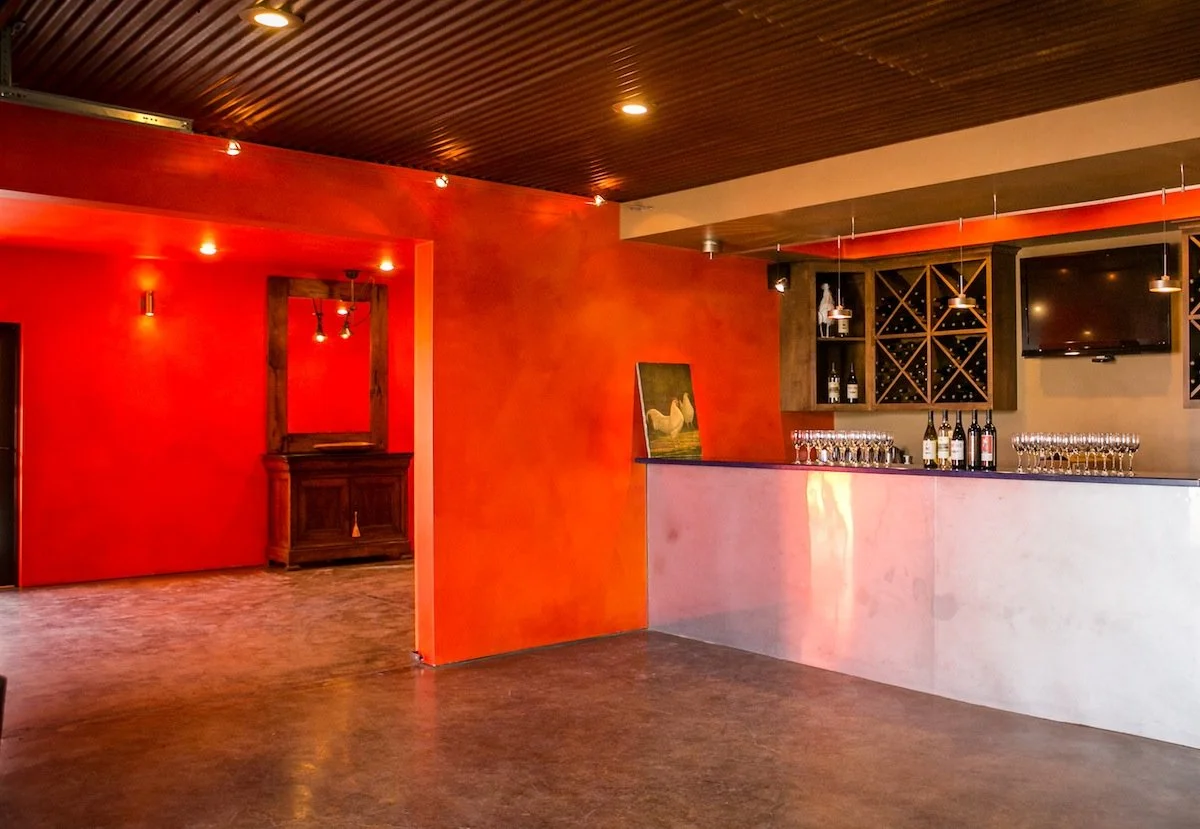Modern wine bar interior with orange walls, polished concrete floors, bottle display, wine glasses, and bar counter