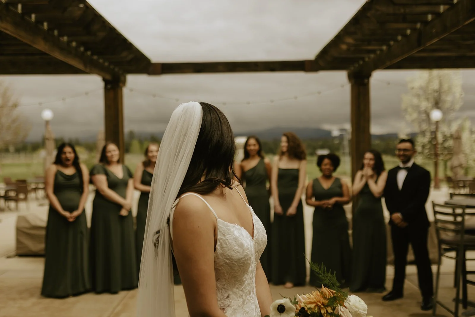 Bride in a white wedding dress and veil holding a bouquet during the toss, with bridesmaids behind her.