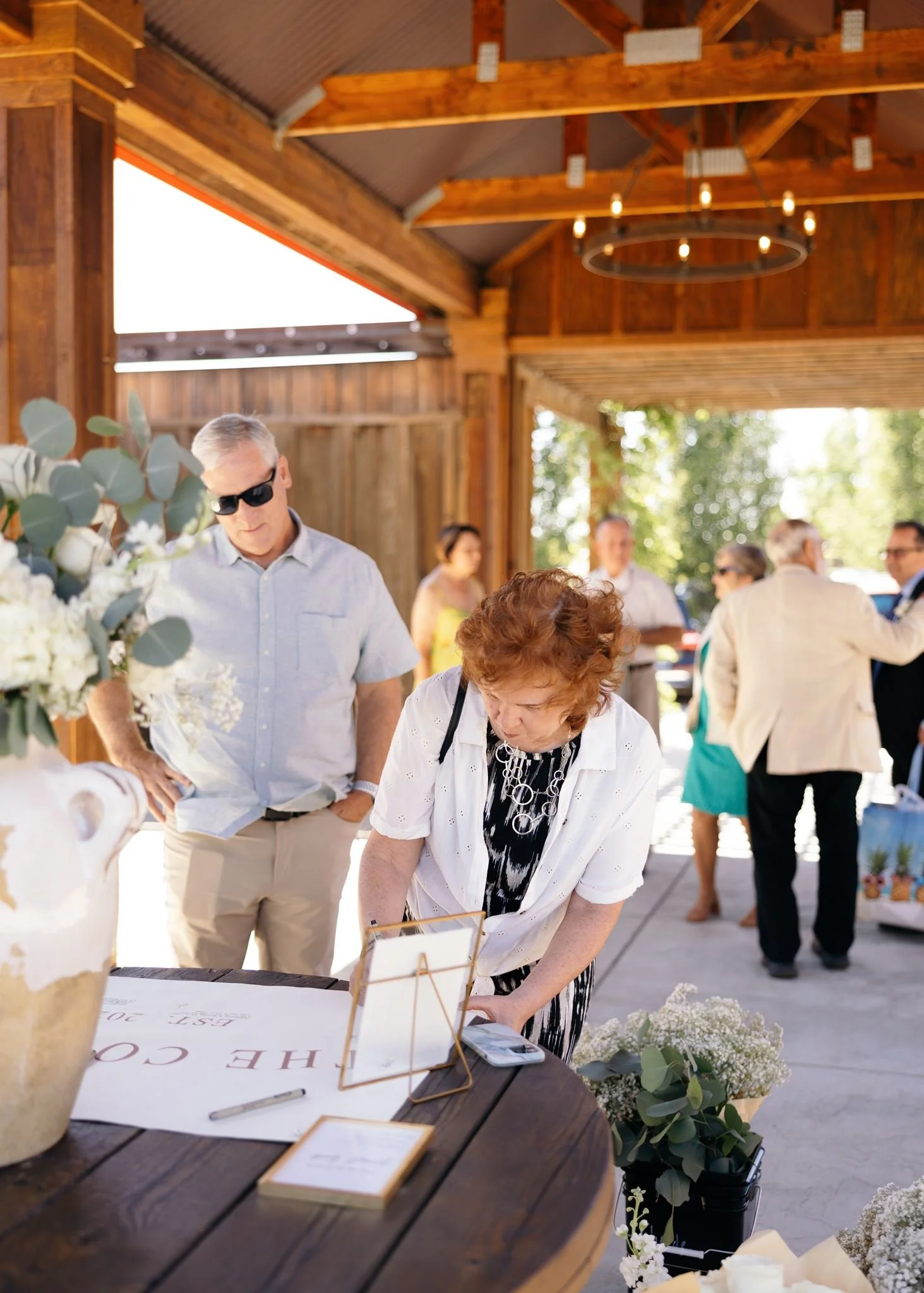 View of Trezzi Farm's Atrium entry area with drapery, wooden beams, custom chandeliers, columns, concrete floor, and a welcome table with white vase--overlooking mountains and vineyards in the distance.